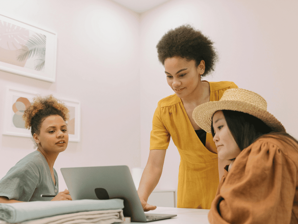 Three diverse women collaborate using a laptop in a bright workspace.