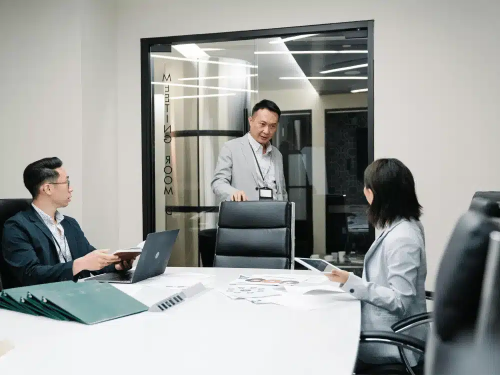 Three business professionals having a meeting in a conference room with glass walls.